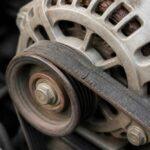 Zbliżenie na alternator samochodowy i zużyty pasek napędowy przy silniku