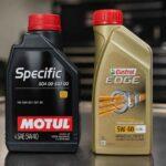 Butelki olejów silnikowych Motul Specific i Castrol Edge 5W-40 na tle warsztatu samochodowego