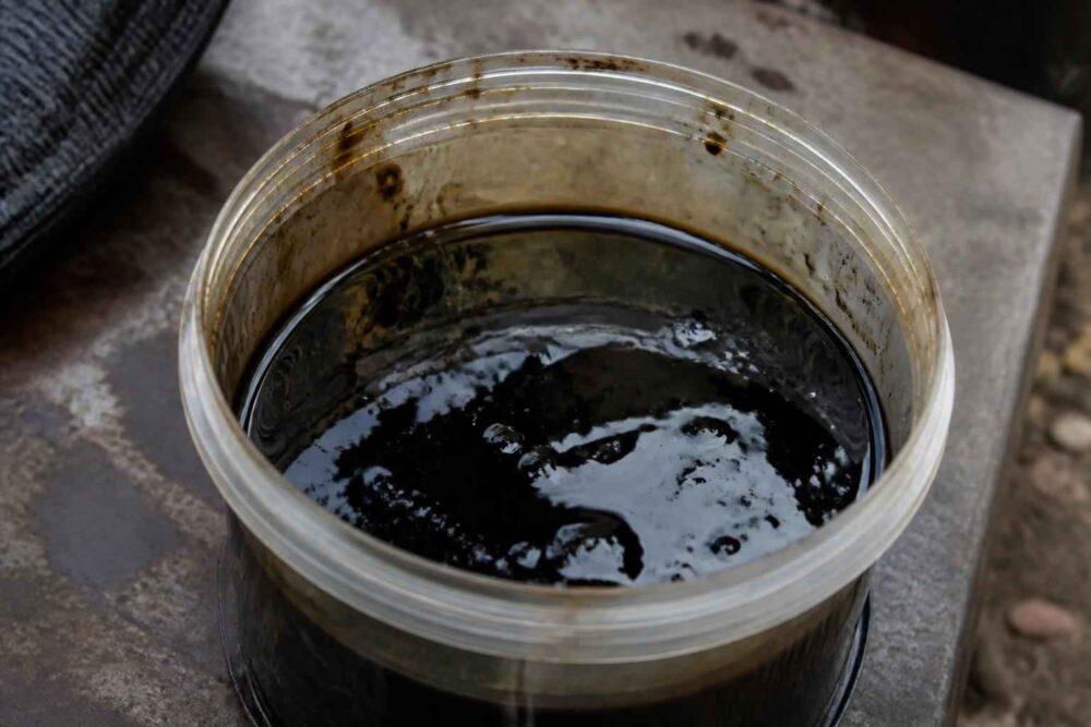 Plastikowy pojemnik wypełniony ciemną, gęstą cieczą na kamiennej powierzchni