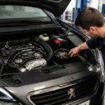 Mechanik w warsztacie sprawdza komorę silnika Peugeota 308 z otwartą maską
