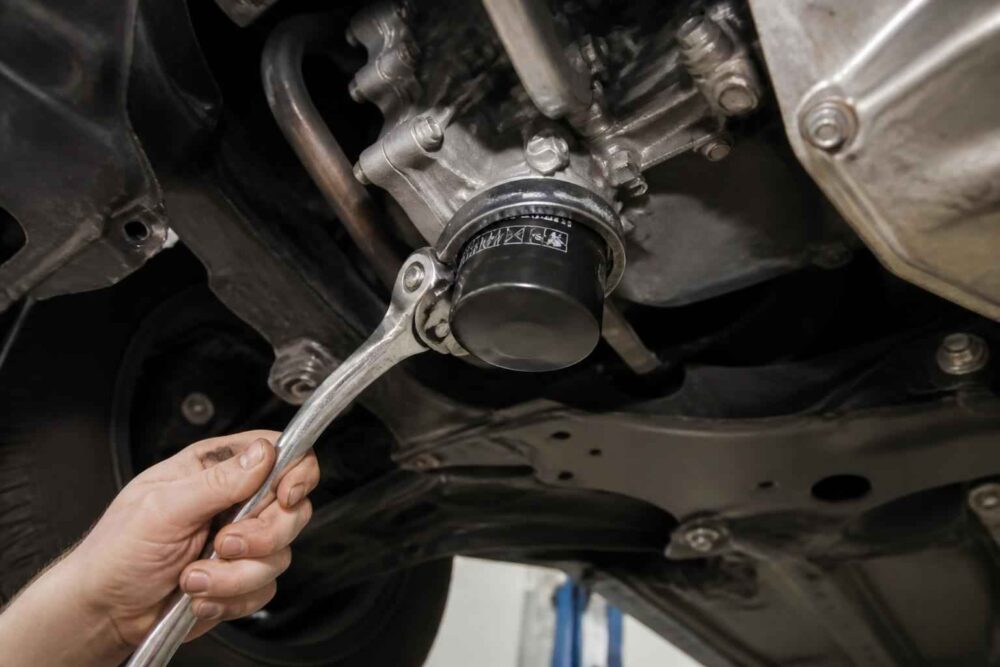 Odkręcanie filtra oleju pod samochodem Mechanik odkręca filtr oleju kluczem taśmowym pod podwoziem samochodu