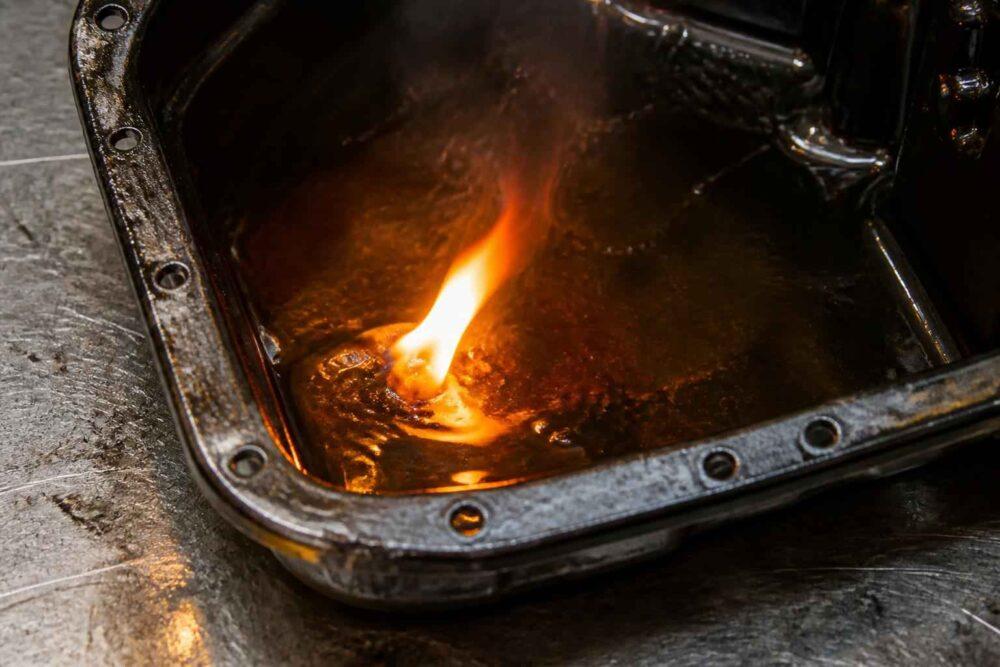 Płomień palącego się oleju w metalowej misce na warsztatowym blacie