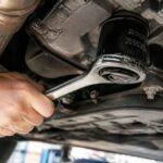 Mechanik odkręca filtr oleju kluczem pod podwoziem samochodu