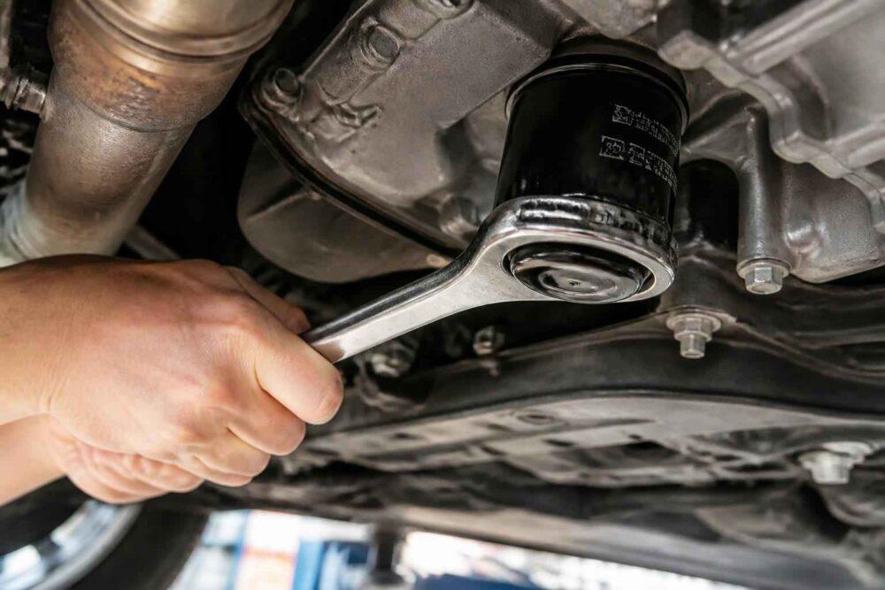 Mechanik odkręca filtr oleju kluczem pod podwoziem samochodu