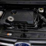 Mechanik trzyma zużyty filtr oleju nad silnikiem samochodu Ford、】【