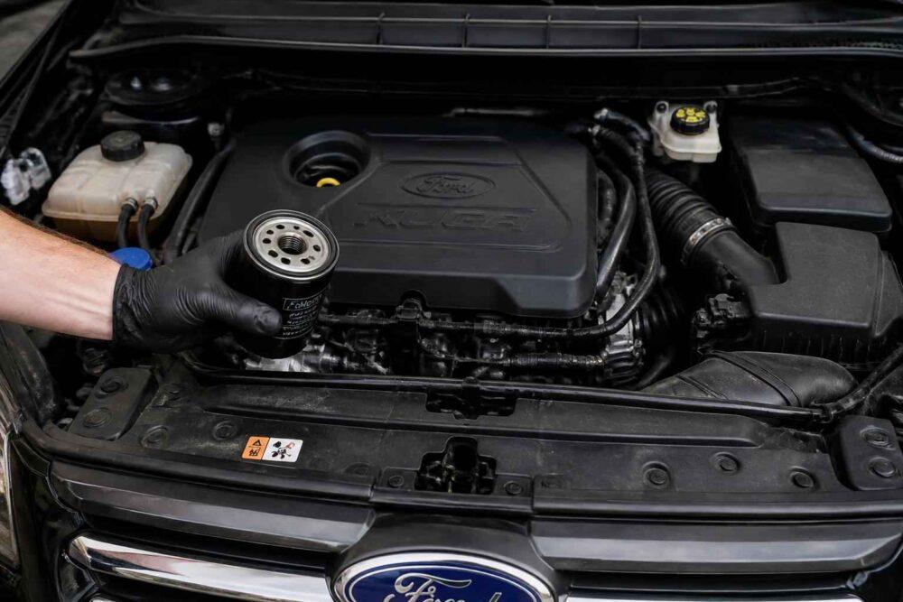 Mechanik trzyma zużyty filtr oleju nad silnikiem samochodu Ford、】【