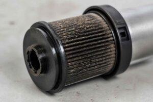 Cylindryczny filtr hydrauliczny z widocznym nagromadzeniem brudu na wkładzie filtracyjnym